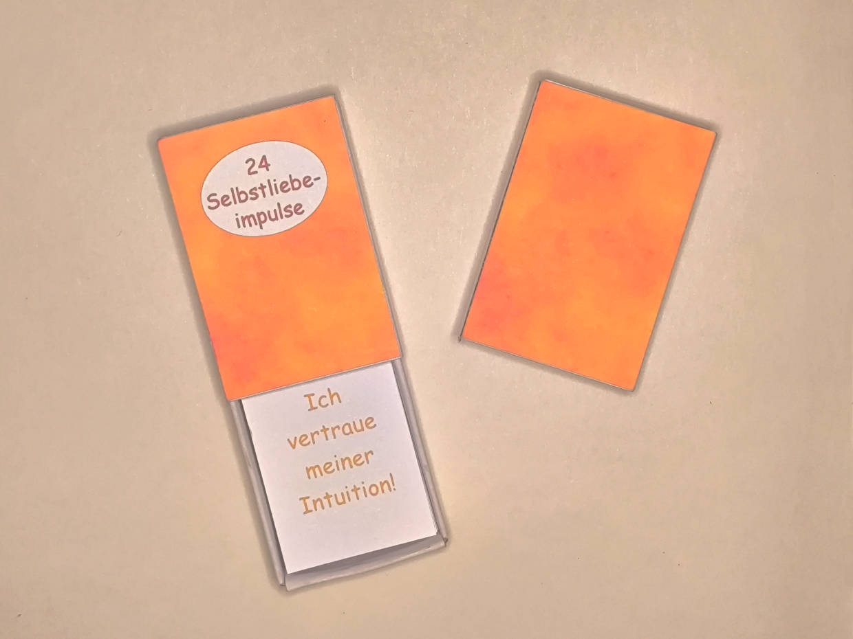 Vorder- und Rückseite der Schatzkiste 24 Selbstliebeimpulse mit einer geöffneter Schachtel für den Blick auf die Impulskärtchen