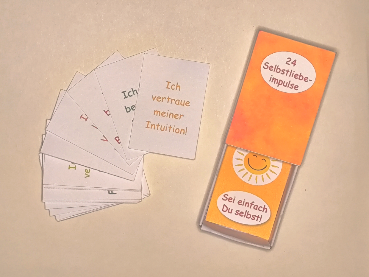 leere geöffnete Schatzkiste 24 Selbstliebeimpulse neben gefächerter Impulskärtchen
